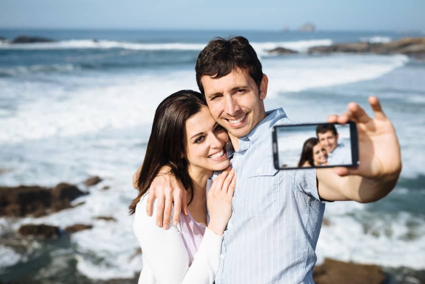 Young couple on honeymoon travel in Asturias coast, Spain, taking selfie portrait photo with smartphone camera.